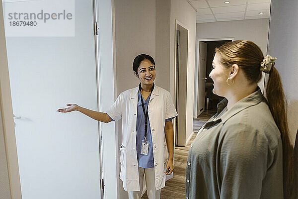 Lächelnder Arzt  der eine Patientin in den Untersuchungsraum einer Klinik begleitet