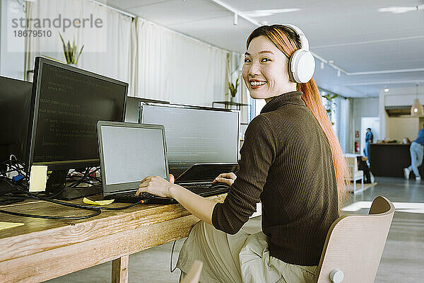 Porträt einer lächelnden Programmiererin  die in einem kreativen Büro am Laptop arbeitet