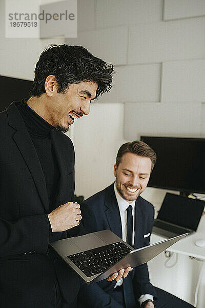 Glücklicher Geschäftsmann  der einen Laptop von einem männlichen Kollegen im Büro hält