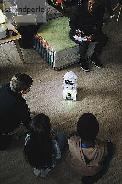 Hochformatige Ansicht von multirassischen Kindern  die vor einem sozialen Roboter im Innovationslabor sitzen