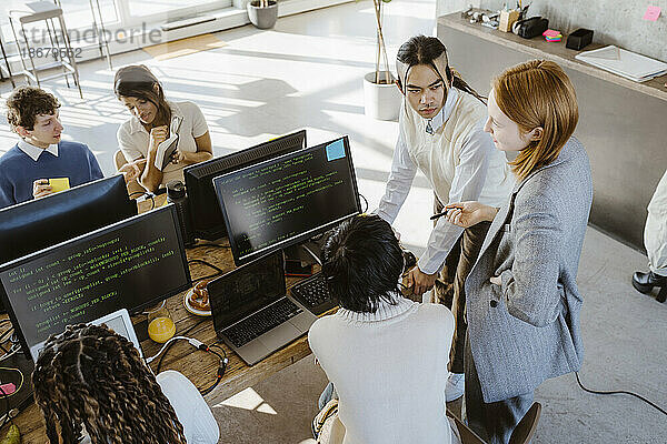 Geschäftsfrau diskutiert mit männlichen und weiblichen Programmierern am Schreibtisch in einem Startup-Büro