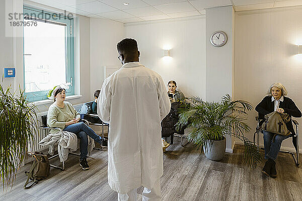 Rückansicht eines männlichen Arztes im Gespräch mit Patienten im Wartezimmer eines Krankenhauses