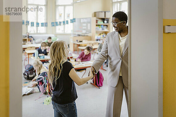 Lächelnde Lehrerin beim Händeschütteln mit Schülerin im Klassenzimmer