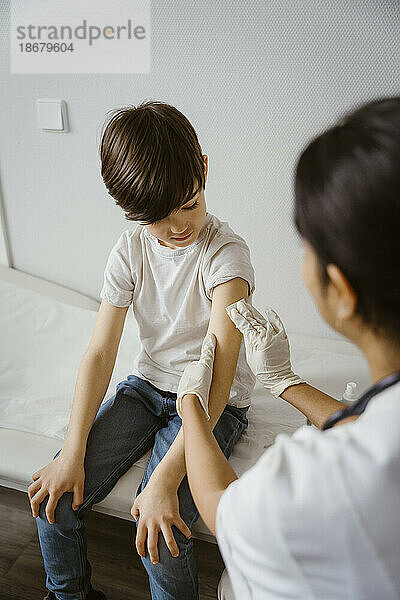 Kinderarzt reinigt den Arm eines Jungen mit einem Alkoholtupfer im Gesundheitszentrum