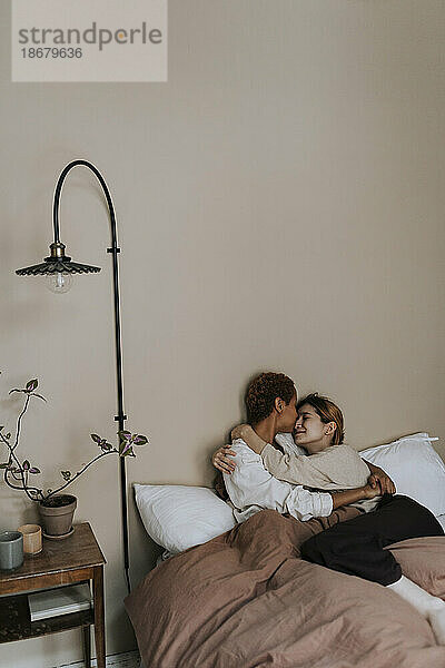 Romantisches nicht-binäres Paar  das zu Hause auf dem Bett liegt