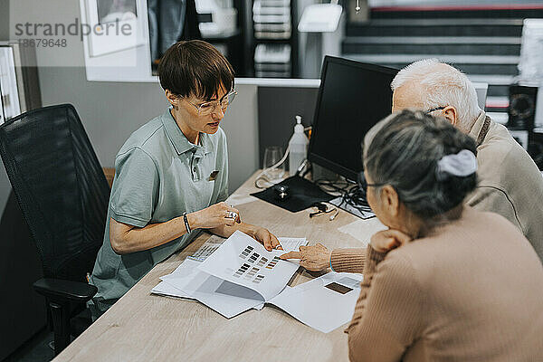 Ein älteres Paar diskutiert mit einer Innenarchitektin über eine Broschüre am Schreibtisch in einem Geschäft
