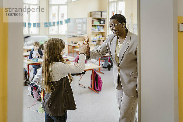 Glückliche Lehrerin gibt einer Schülerin  die an der Tür steht  ein High-Five