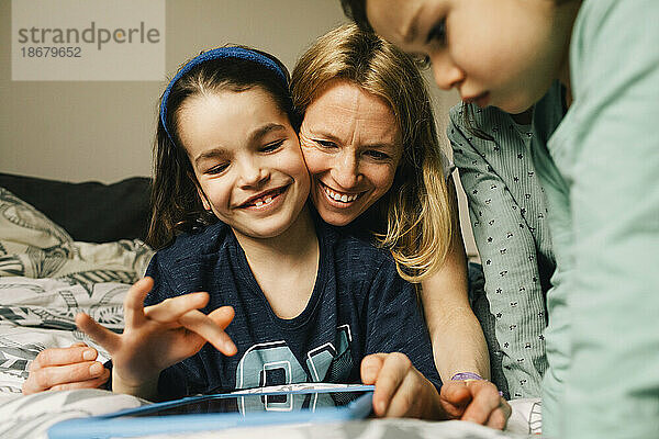 Glückliche Frau mit Söhnen  die zu Hause ein digitales Tablet benutzen