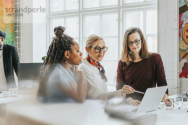 Geschäftsfrau  die auf einen Laptop zeigt  während sie mit weiblichen Kollegen im Büro diskutiert