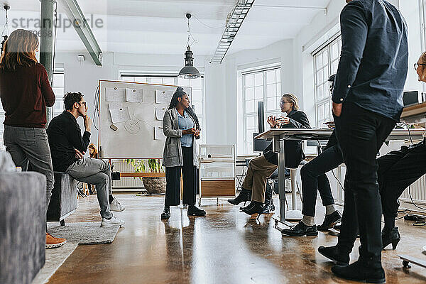 Gemischtrassige Kollegen hören einer Geschäftsfrau zu  die bei einem Treffen im Büro ihre Strategie erläutert