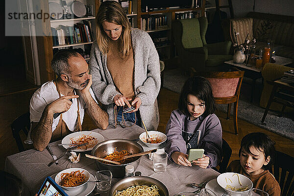 Familie mit Spaghetti und Smartphones am Esstisch