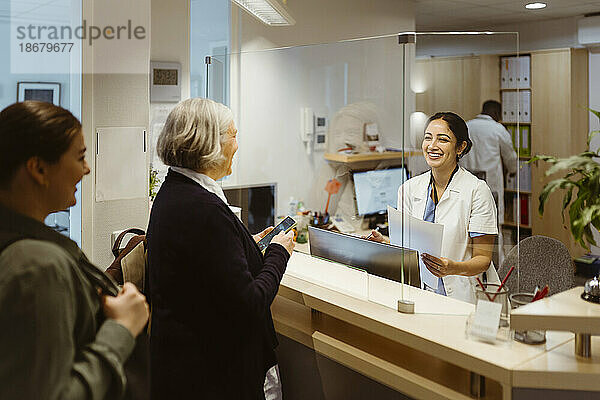 Patienten im Gespräch mit einer Empfangsdame durch ein transparentes Schild in einer Klinik