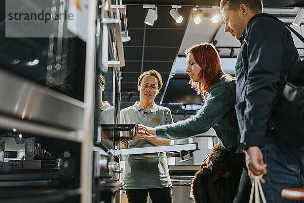 Weibliche Verkäuferin  die einem reifen Paar beim Kauf eines Mikrowellenofens in einem Elektronikgeschäft hilft