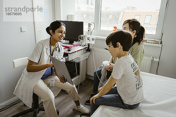 Kinderärztin im Gespräch mit Mutter und Sohn über Tablet-PC im Untersuchungsraum einer Klinik