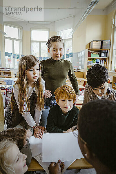 Jungen und Mädchen betrachten den Lehrer  der ihnen im Klassenzimmer hilft