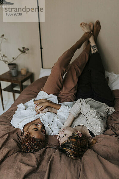 Nicht-binäres Paar verbringt seine Freizeit entspannt auf dem Bett zu Hause