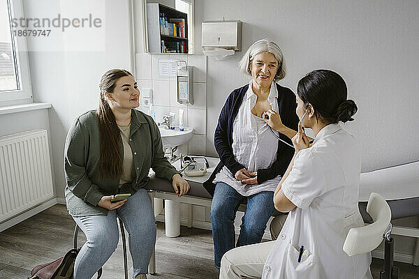 Arzt hört den Herzschlag einer älteren Frau ab  die mit ihrer Tochter in der Klinik sitzt