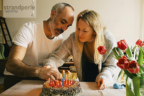 Paar arrangiert Kerzen auf Geburtstagskuchen zusammen zu Hause