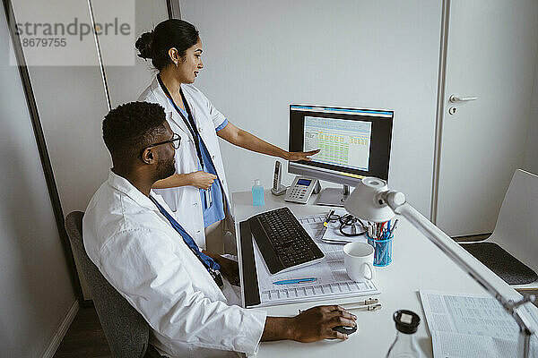 Eine Ärztin erklärt einem männlichen Kollegen am Desktop-PC im Gesundheitszentrum die Strategie