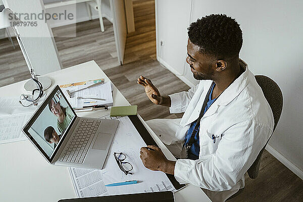 Hoher Blickwinkel eines männlichen Kinderarztes  der Patienten per Videoanruf auf einem Laptop im Gesundheitszentrum begrüßt