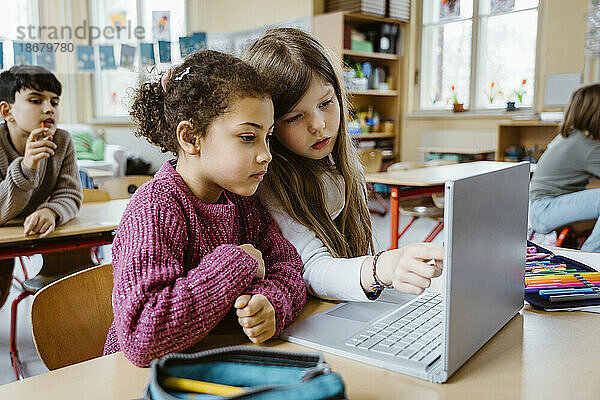 Schulmädchen teilen sich gemeinsam einen Laptop am Schreibtisch im Klassenzimmer