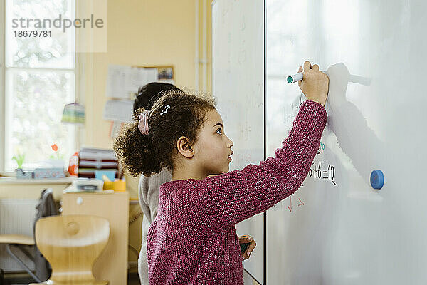 Seitenansicht eines Mädchens und eines Jungen  die auf einer Tafel im Klassenzimmer schreiben