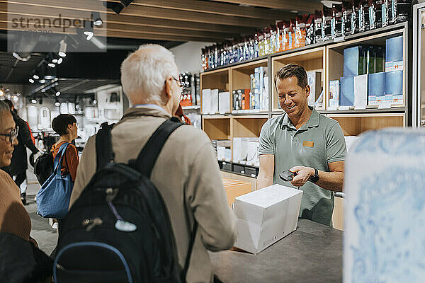 Lächelnde Verkäuferin beim Scannen eines Gerätekastens  während Kunden an der Kasse eines Elektronikgeschäfts stehen