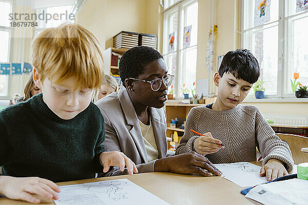 Lehrer hilft Jungen beim Lösen von Problemen  während sie am Schreibtisch im Klassenzimmer sitzen