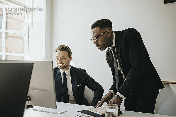 Männliche Unternehmer  die am Schreibtisch im Büro über einen Desktop-PC diskutieren