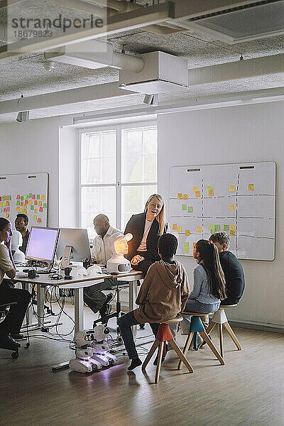 Lehrerin diskutiert mit multirassischen Schülern  die vor einem sozialen Roboter im Innovationslabor sitzen