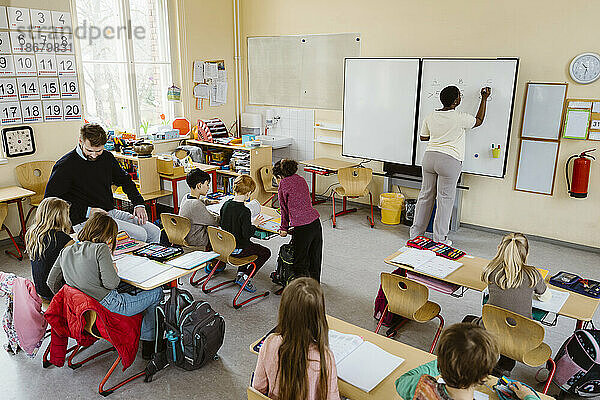 Männlicher und weiblicher Lehrer unterrichten Schüler am Schreibtisch sitzend im Klassenzimmer