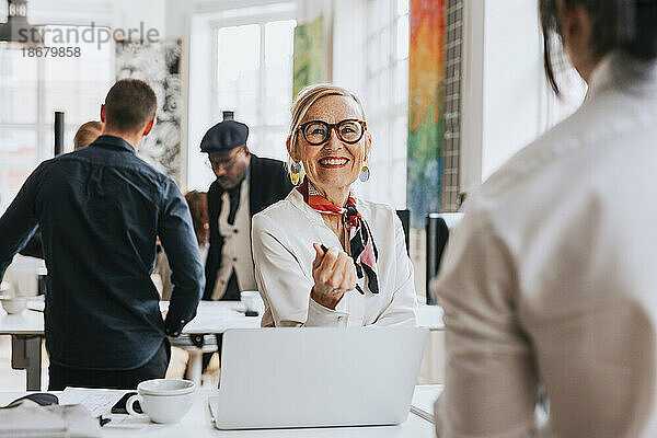 Glückliche Geschäftsfrau mit Brille im Gespräch mit einem Kollegen im Büro