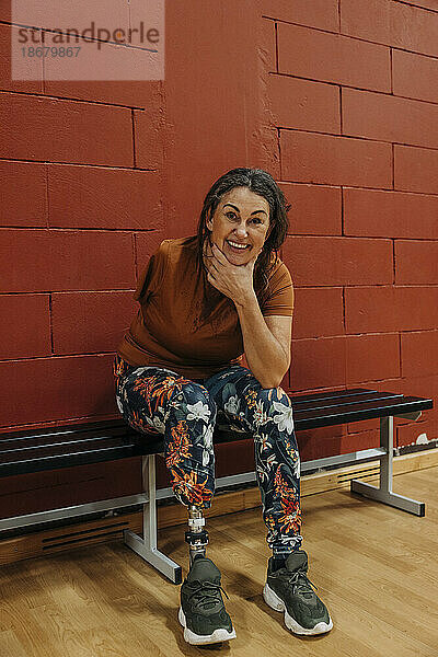 Porträt einer glücklichen Sportlerin mit amputiertem Bein  die auf einer Bank auf einem Sportplatz sitzt
