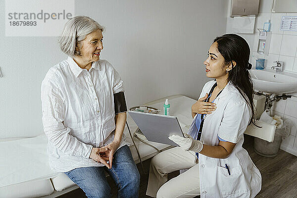 Ärztin hält Tablet-PC und berät einen älteren Patienten  der in einer Klinik auf dem Bett sitzt