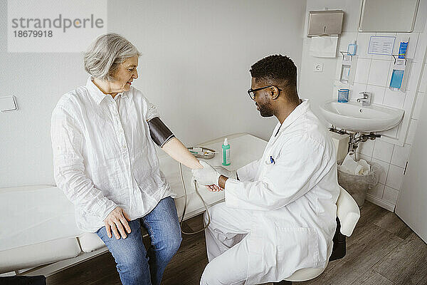 Junger männlicher Arzt  der in einer Klinik den Blutdruck einer Patientin kontrolliert