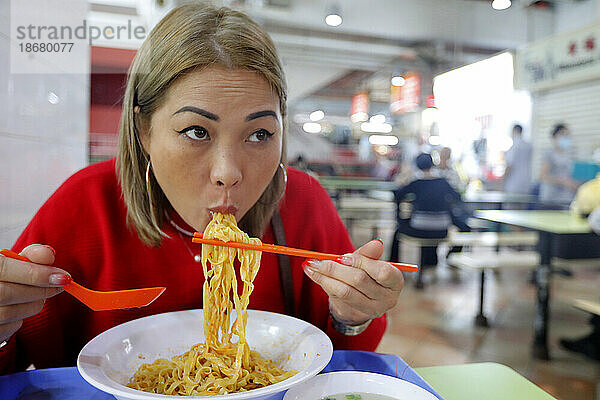 Young woman eating at traditional Asian food stall in Singapore Food Trail hawker center  Singapore  Southeast Asia  Asia