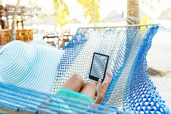 Frau liest auf einem Kindle-Tablet und liegt auf einer Hängematte  Sansibar  Tansania  Ostafrika  Afrika