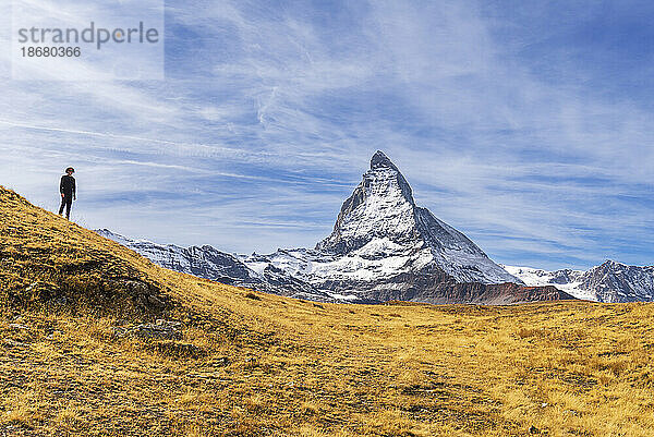 Wanderer steht vor der ikonischen Form des Matterhorns inmitten gelber Gräser  Riffelalp  Zermatt  Kanton Wallis  Schweizer Alpen  Schweiz  Europa