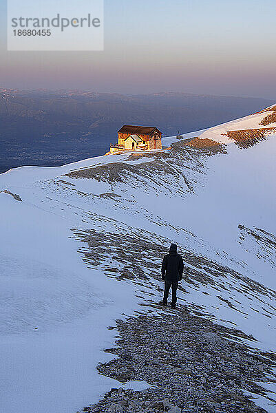 Winteransicht eines Wanderers  der den Sonnenuntergang in der Berghütte Duca degli Abruzzi  Campo Imperatore  Apennin  Bezirk L'Aquila  Abruzzen  Italien  Europa bewundert