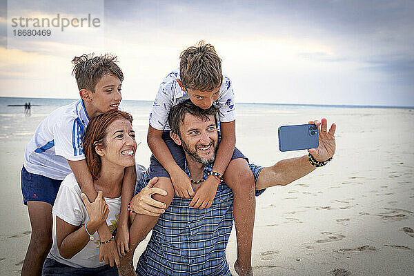 Glückliche Familie mit zwei Jungen  die am Strand von Sansibar  Tansania  Ostafrika  Afrika ein Selfie mit dem Smartphone machen