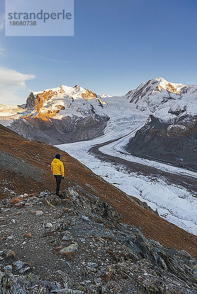 Wanderer steht auf Felsen und bewundert das Monte-Rosa-Massiv  den Gornergletscher und die Lyskamm-Gipfel bei Sonnenuntergang  Riffealp  Zermatt  Kanton Wallis  Schweizer Alpen  Schweiz  Europa