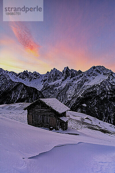 Einsame Berghütte im Tiefschnee mit majestätischen Gipfeln im Hintergrund im Morgengrauen  Tombal  Val Bregaglia  Graubünden  Schweiz  Europa