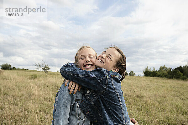 Lächelnde Freundinnen (10-11) umarmen sich im Feld