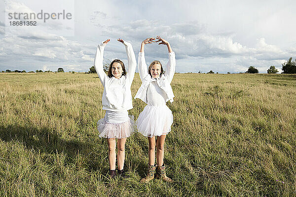 Lächelnde Freundinnen (10-11) machen Ballettpose im Feld
