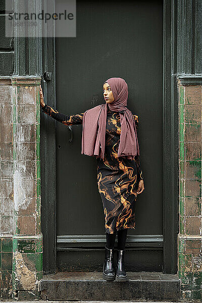 Junge Frau im Hijab steht vor heruntergekommenem Gebäude