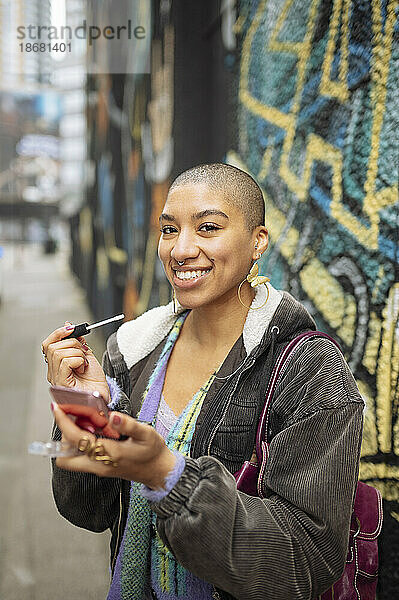 Porträt einer jungen Hipster-Frau  die auf der Straße Lipgloss aufträgt