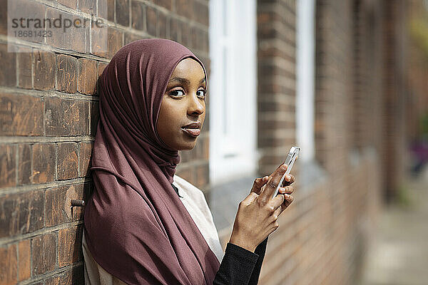 Porträt einer jungen Frau im Hijab  die ihr Telefon benutzt