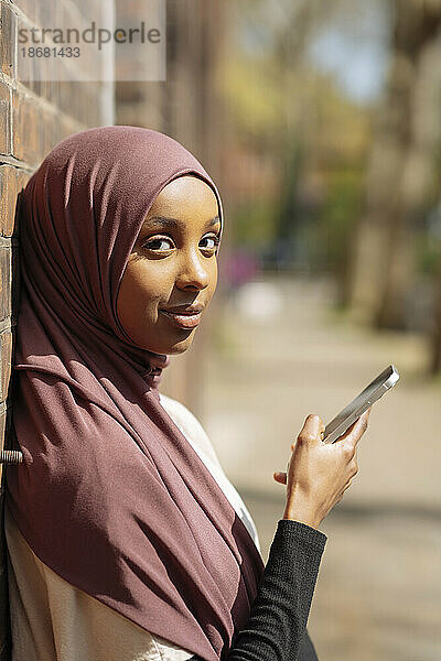 Porträt einer jungen Frau im Hijab  die ihr Telefon benutzt