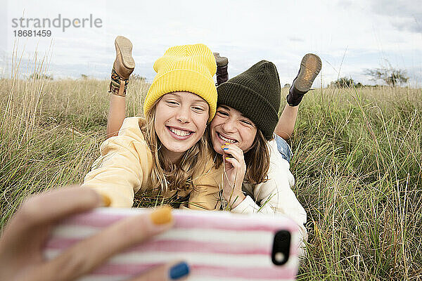 Lächelnde Freundinnen (10-11) liegen im Gras und machen ein Selfie