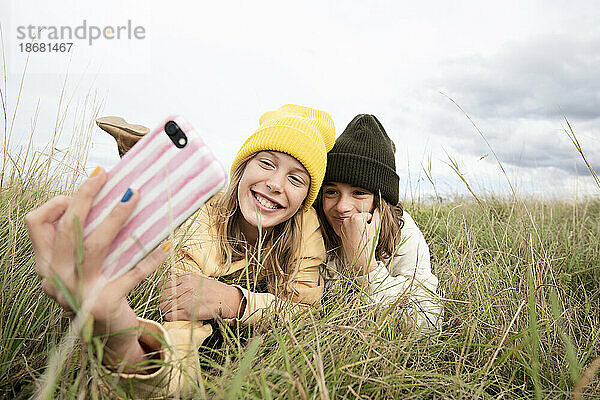 Lächelnde Freundinnen (10-11) liegen im Gras und machen ein Selfie